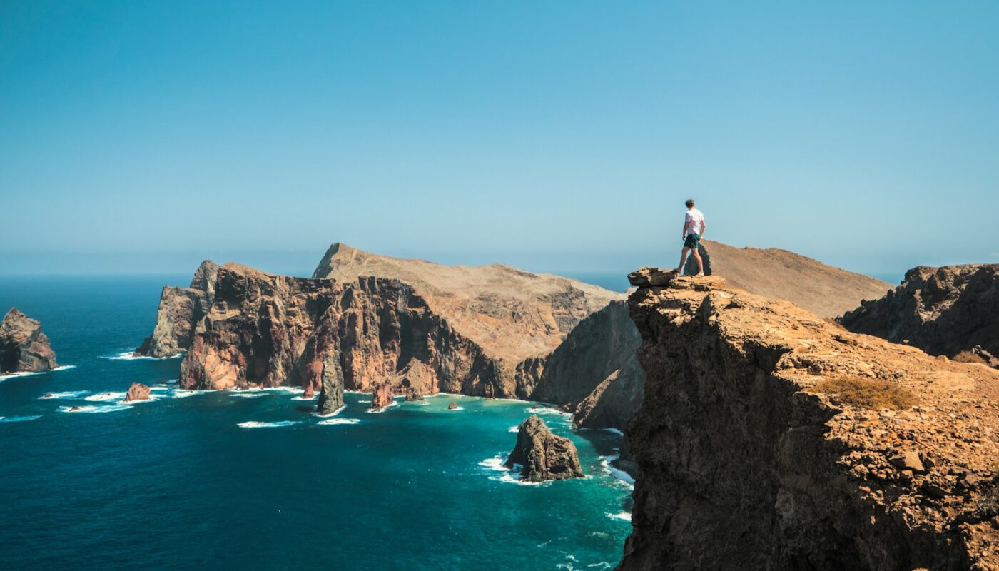 man standing on brown rock formation near blue sea during daytime